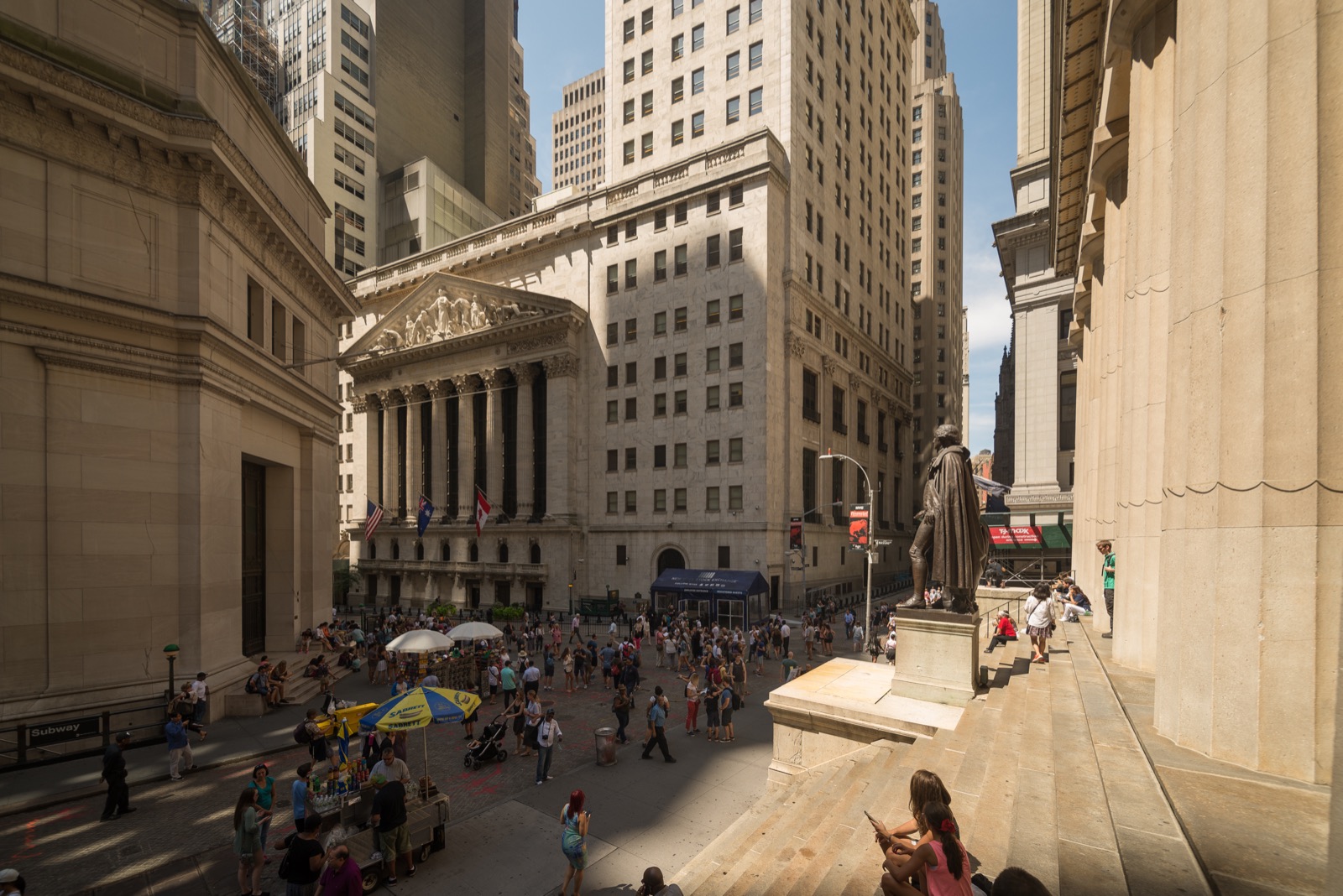 The facade of the New York Stock Exchange building on Wall Street, with its columns and a large American flag.