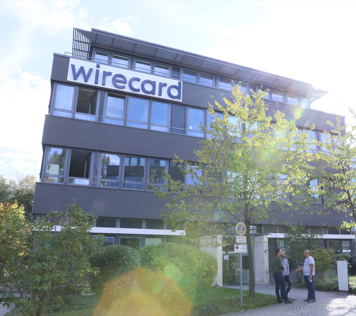 The headquarters of Wirecard in Aschheim, near Munich, Germany — a modern office building with the blue 'wirecard' logo across its upper facade, on a sunny day.